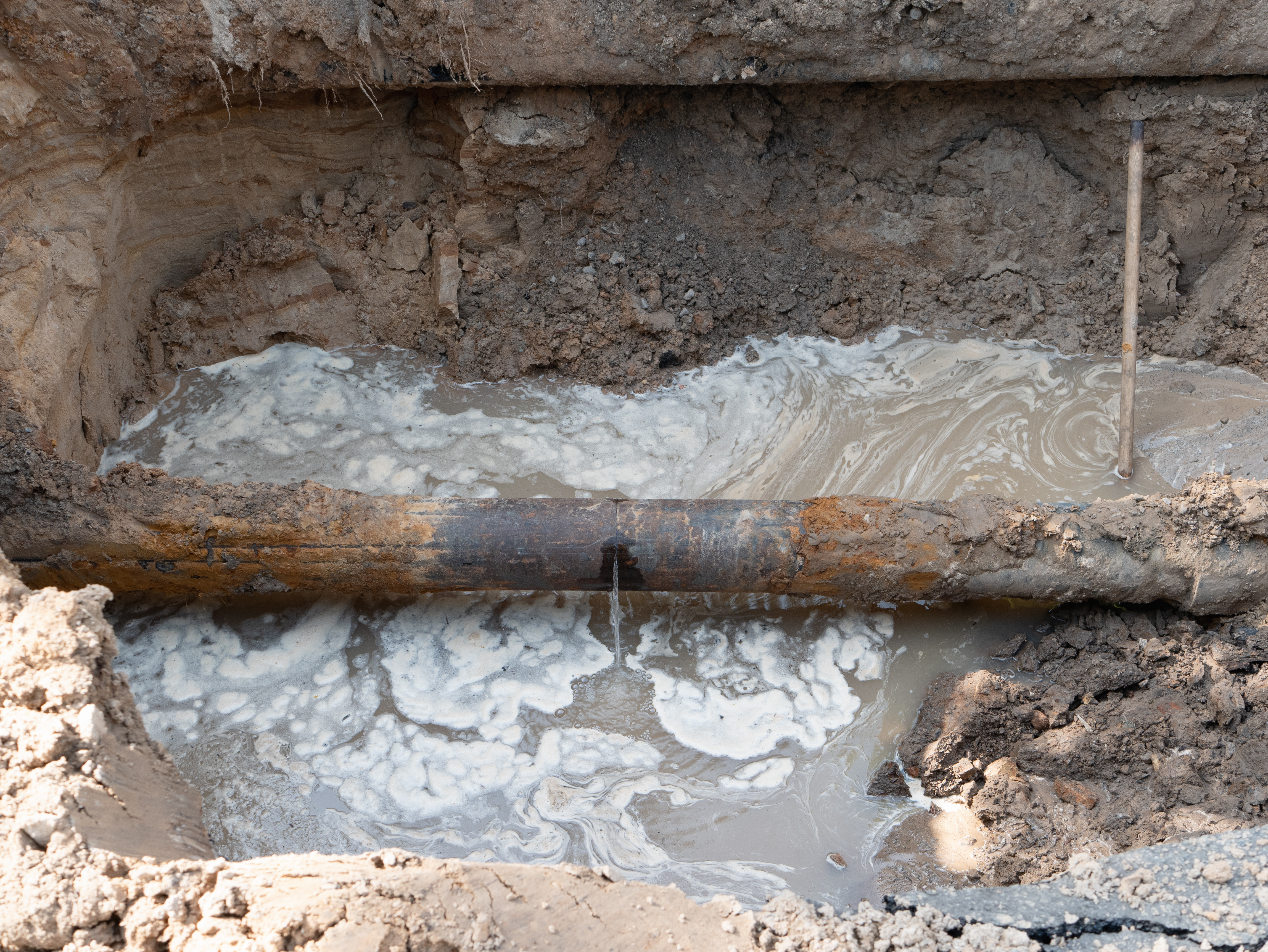 A cracked underground pipe with a second water line running just above it in the same trench