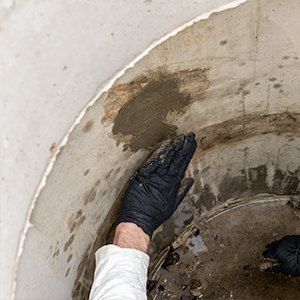 Gloved hand pressing Strong-Plug into a leak in a concrete manhole