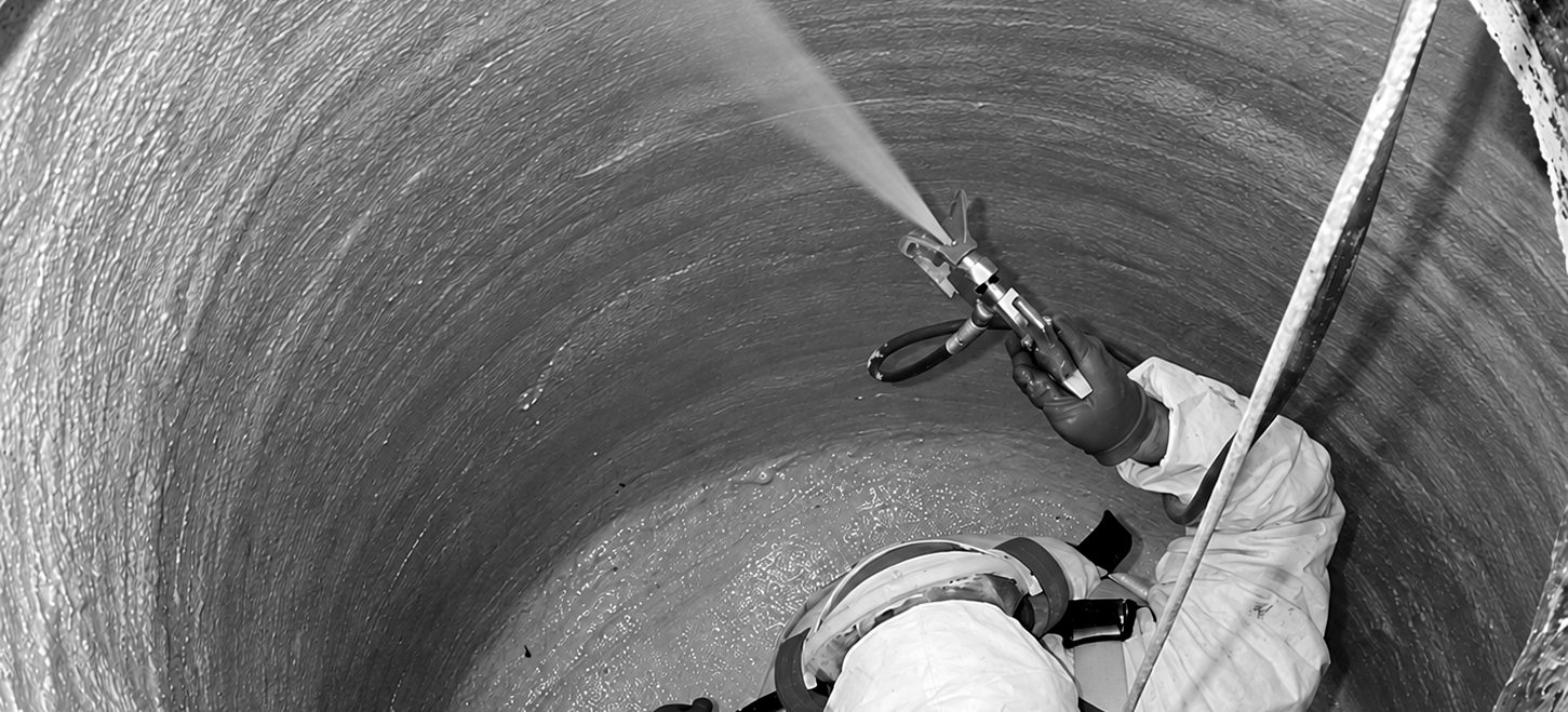 A worker in a harness spraying a cementitious liner onto the inside wall of a manhole