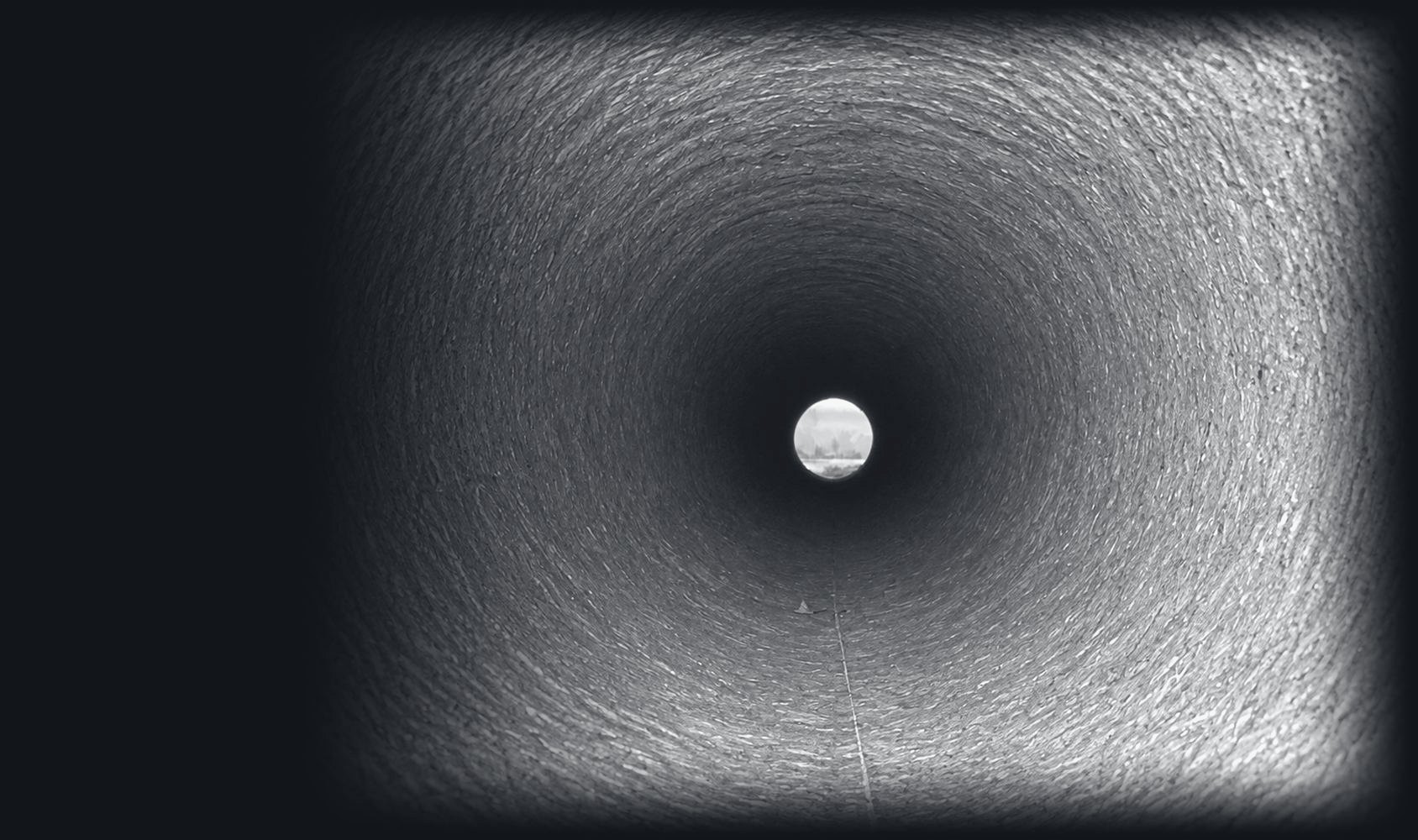 Looking down the inside of a large concrete pipe toward daylight