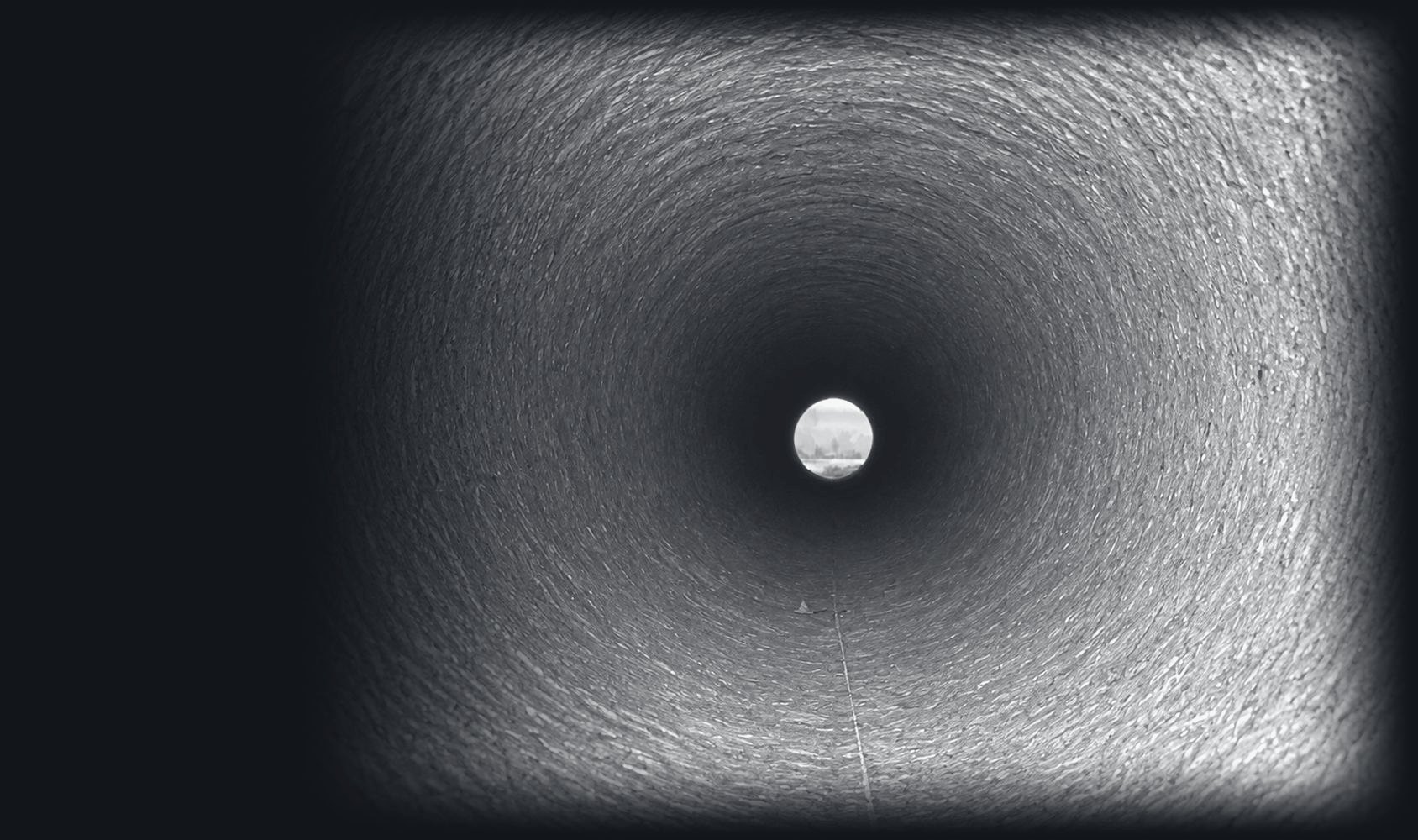 Looking down the inside of a large concrete pipe toward daylight