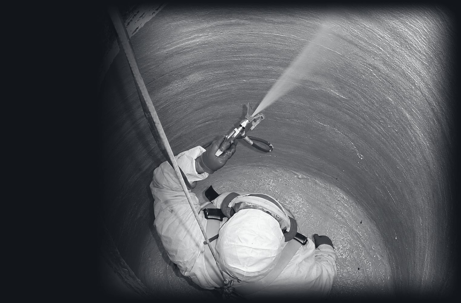 A worker in a harness spraying a cementitious liner onto the inside wall of a manhole
