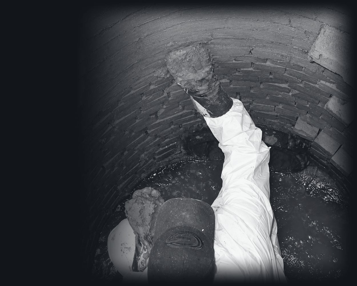 A gloved hand pressing leak-stop cement into a brick manhole wall