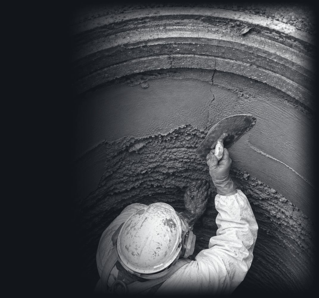 A worker troweling repair mortar onto the inside wall of a manhole