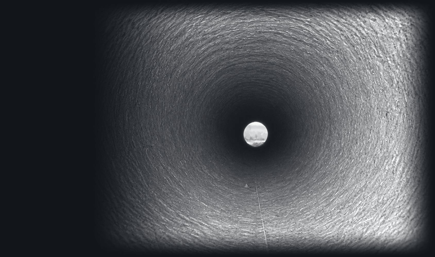 Looking down the inside of a large concrete pipe toward daylight