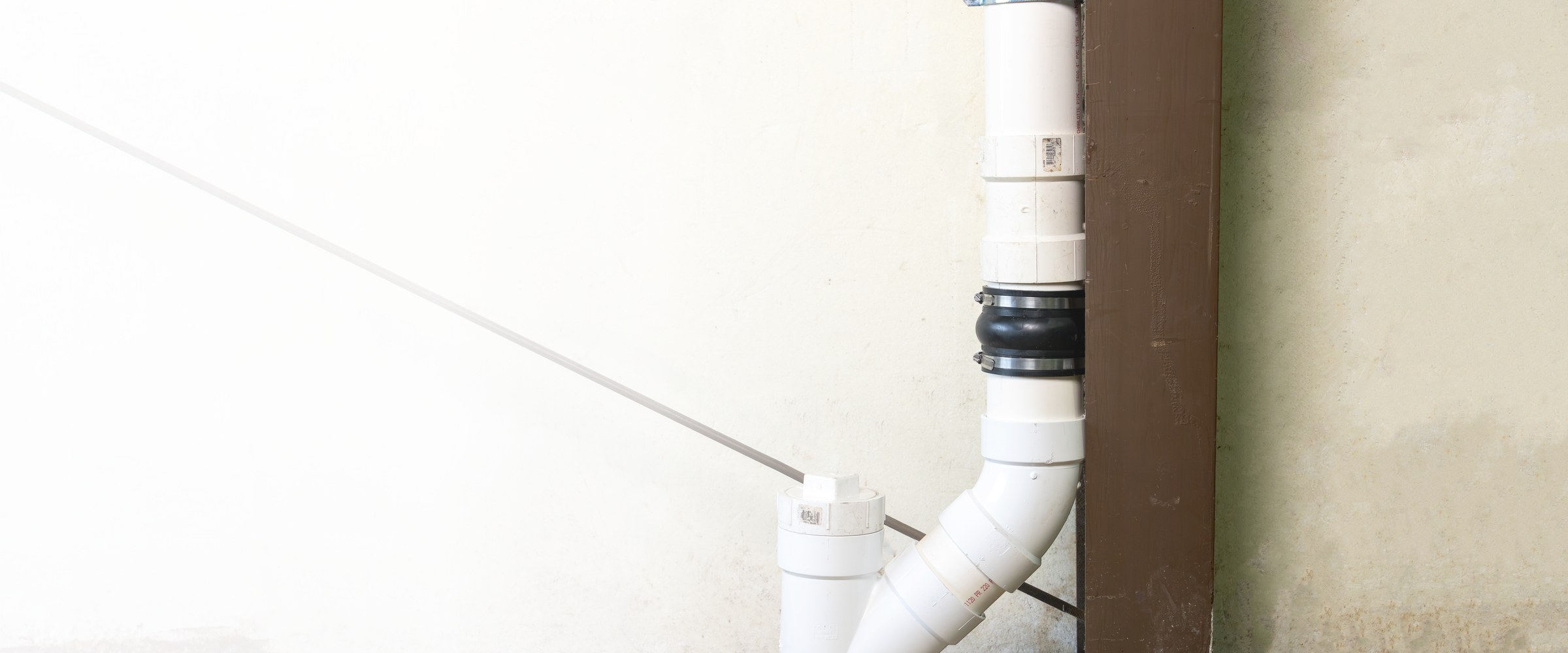 Fernco Expansion Joint installed on a vertical white PVC DWV stack above a wye and cleanout